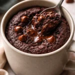 Delicious brownie in a mug served with chocolate drizzle and a spoon.