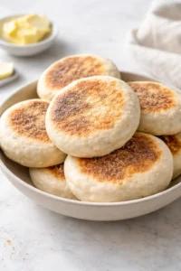 Homemade sourdough English muffins, golden brown and fluffy, on a kitchen table.