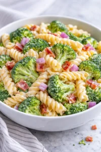 A colorful bowl of fresh broccoli pasta salad with cherry tomatoes and dressing