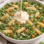 Bowl of vibrant Kale Caesar Pasta Salad with croutons and dressing